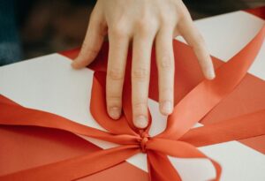 A hand unwraps a gift box with a red ribbon, symbolizing celebration and surprise.